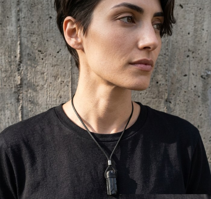 The raw tourmaline necklace worn over a black tee against a concrete wall