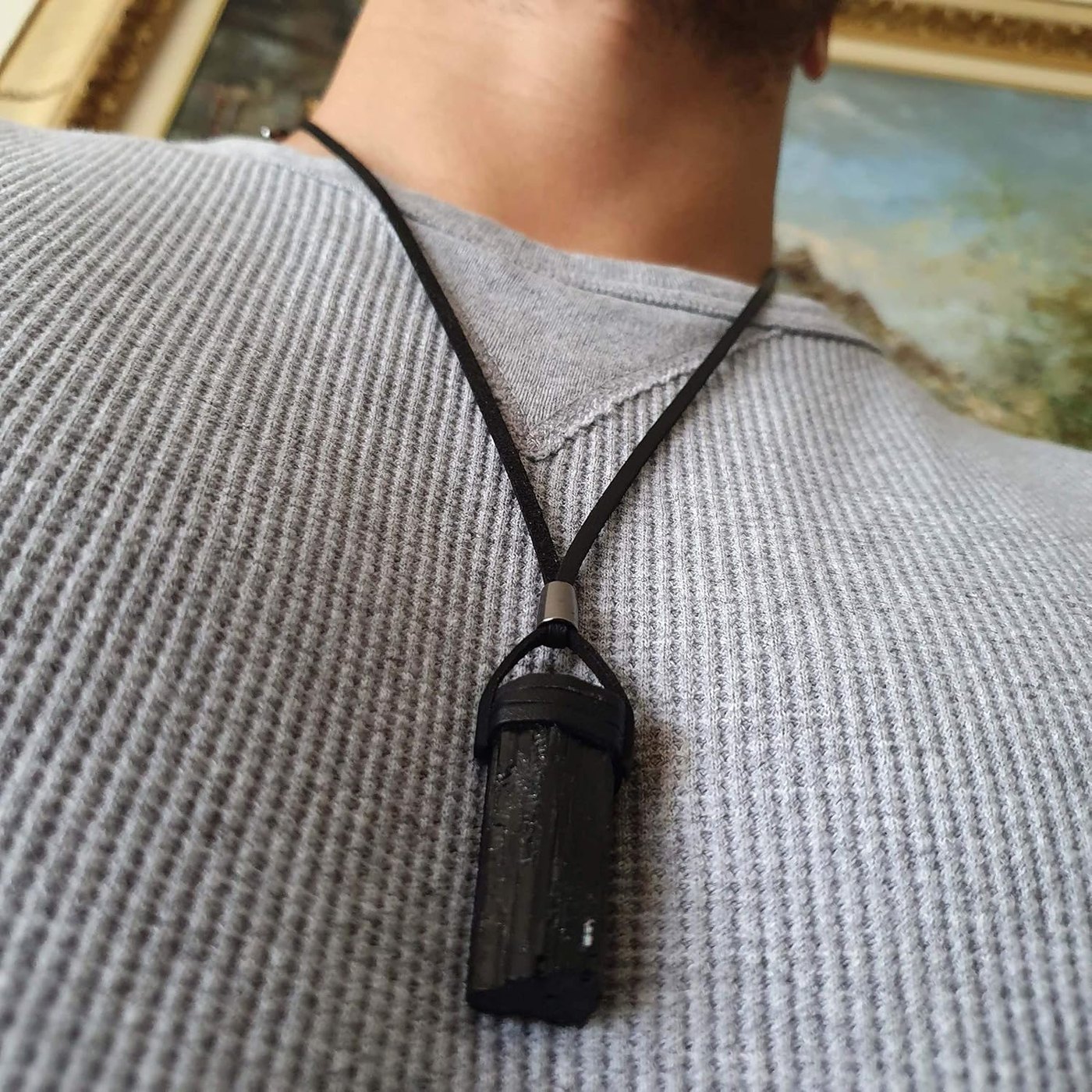 Raw black tourmaline necklace worn on the chest over a grey knit shirt